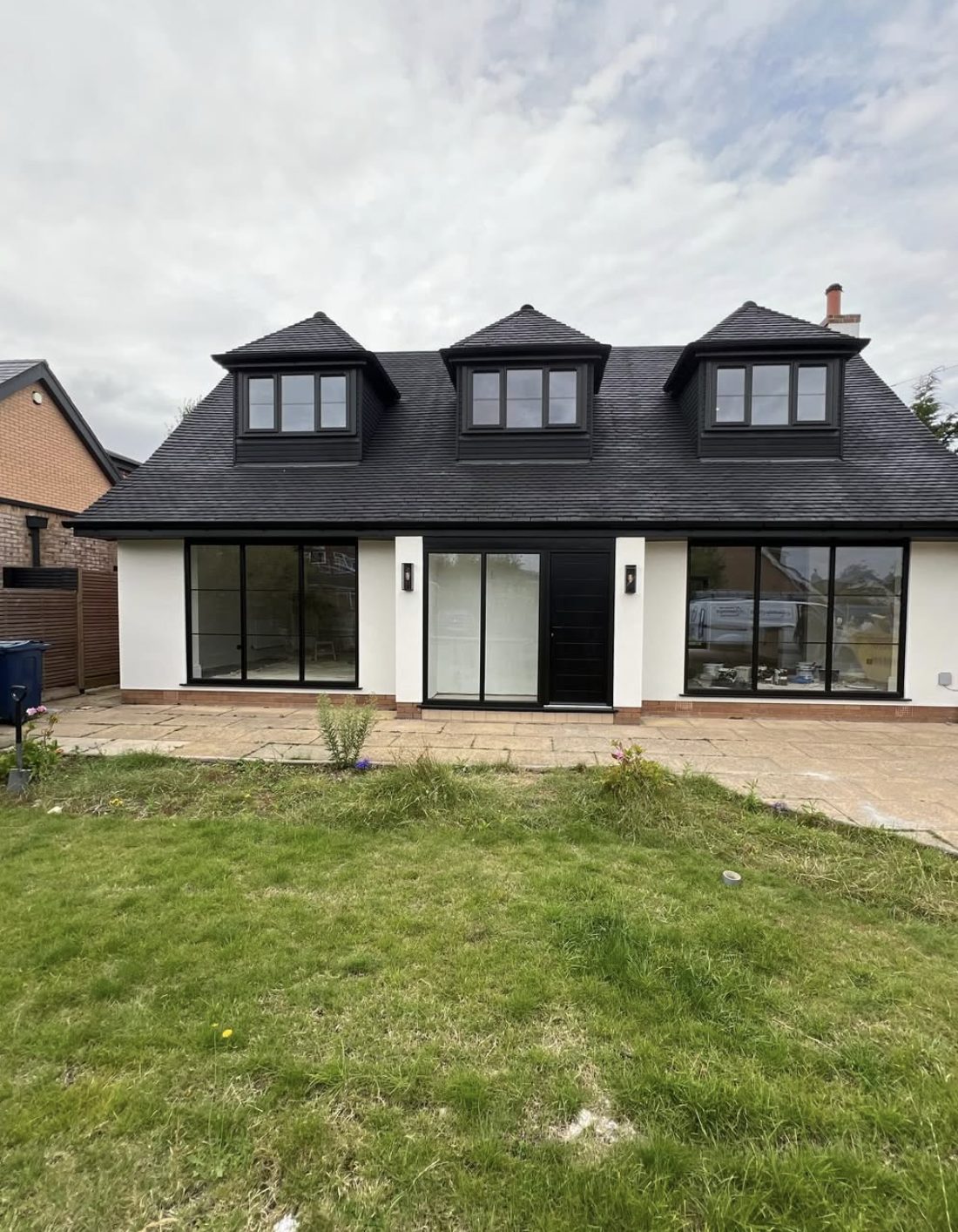 Rear of a chalet bungalow in white render with three dormers and wide glazing